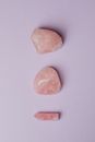 在柔软的紫色背景上，一组由三块玫瑰石英石构成的简约组合，展现了其自然之美
