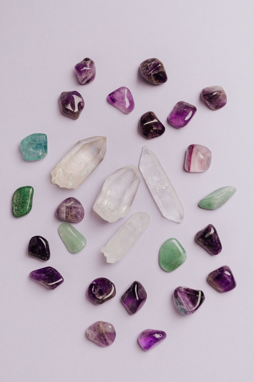 Tumbled amethyst, fluorite and quartz points laid out on a pale surface, photo by Kaboompics.com on Pexels