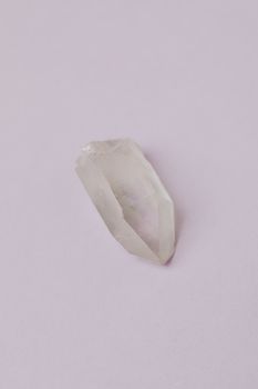 A clear quartz crystal on a light pastel surface, showcasing its natural beauty and texture.