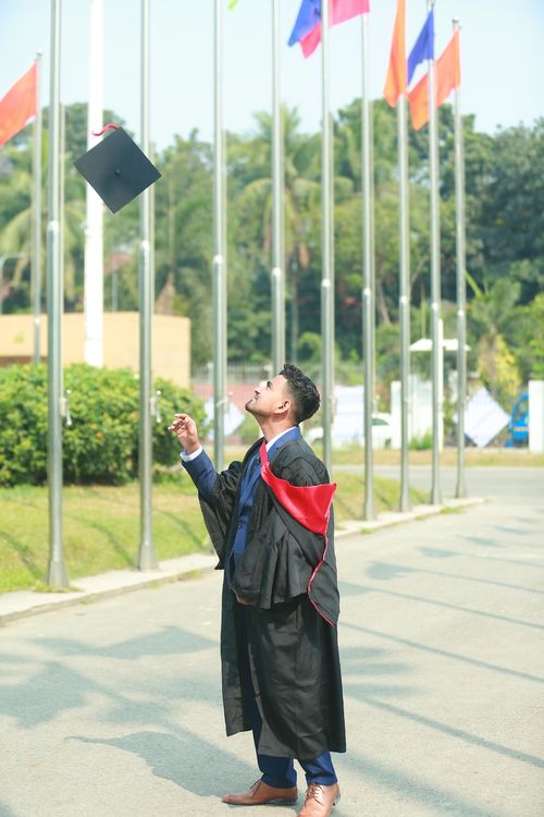 Free Graduate celebrates by tossing cap into the air outside. Joyful success moment. Stock Photo