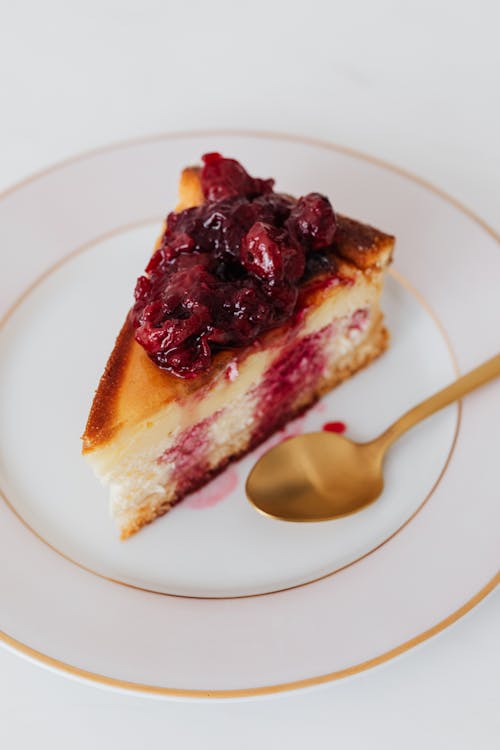 Free Slice of cheesecake topped with cherry compote on white plate with gold spoon. Stock Photo