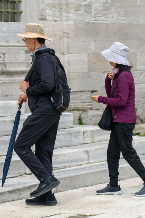 Free Two adults wearing hats and jackets walking up stone steps outdoors. Stock Photo