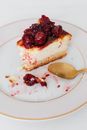 From above closeup of bitten piece of yummy homemade cheesecake garnished by cherry jam on plate served with spoon