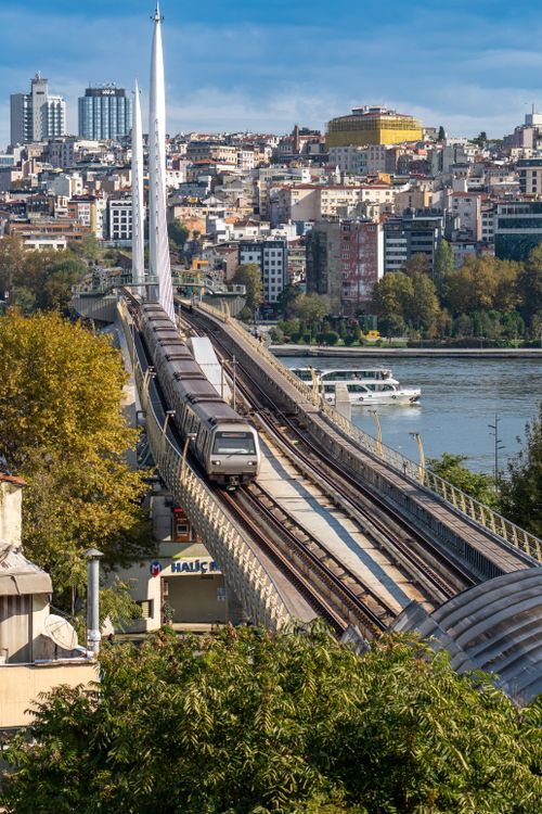 Free A metro train crosses a bridge over a river in a bustling city setting, with high-rises on the skyline. Stock Photo