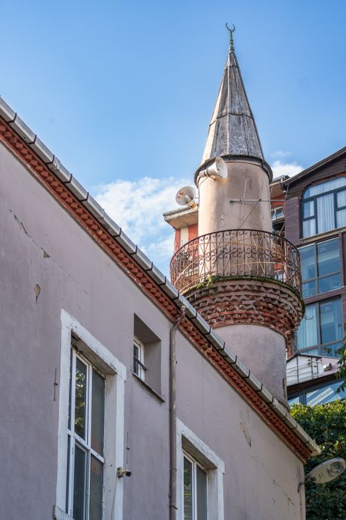 Free A historic minaret with a crescent moon atop rises beside a traditional building under a bright blue sky. Stock Photo