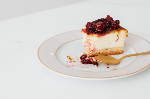 Free From above of bitten piece of homemade cheesecake garnishing with berry jam placed on plate with spoon Stock Photo