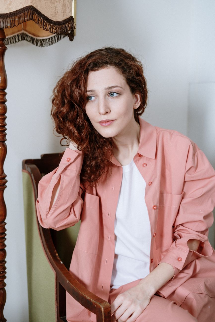 Portrait of a red-haired woman sitting indoors, embracing a cozy home vibe.