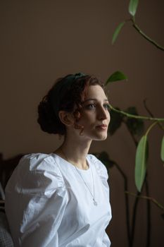 Portrait of a woman with curly hair in a white blouse indoors, exuding serenity.