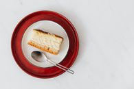 Top view of piece of classic cheesecake served on plate with spoon on white surface