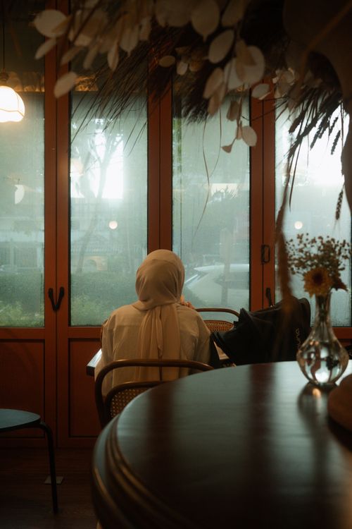 Free Serene cafe interior with a woman seated by a window, evoking tranquility. Stock Photo
