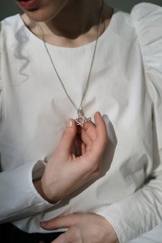 特写一个女人手拿白色上衣上的大卫之星项链