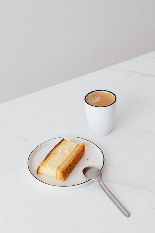 Free From above of hot cappuccino on white marble surface with fresh delicious piece of cake and tea spoon Stock Photo