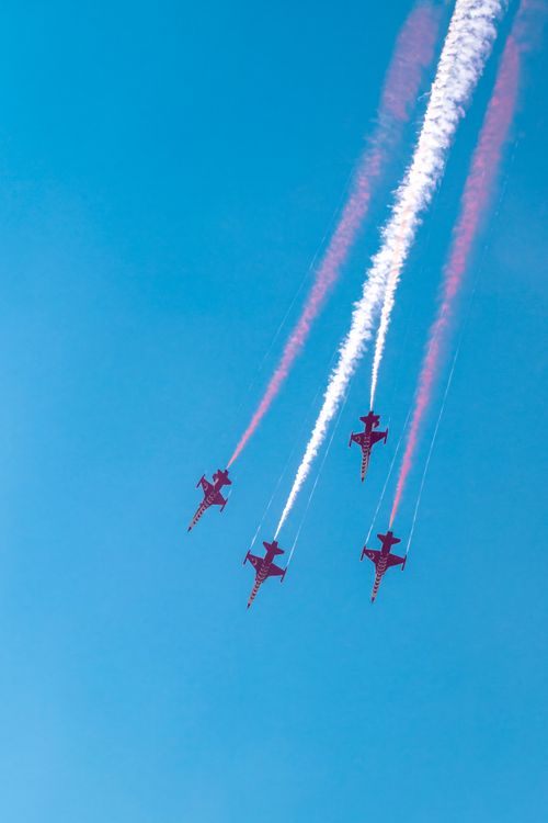 Free Four aerobatic airplanes creating colorful smoke trails against a bright blue sky. Stock Photo