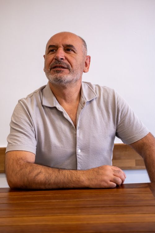Free A pensive middle-aged man with a beard sits indoors by a wooden table. Stock Photo
