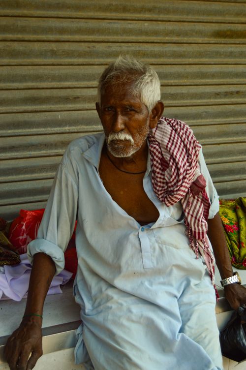 Free Old man resting in traditional attire with checkered shawl against a corrugated backdrop. Stock Photo