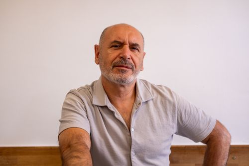 Free A mature man in a casual shirt sits confidently in a cafe setting, exuding a relaxed demeanor. Stock Photo