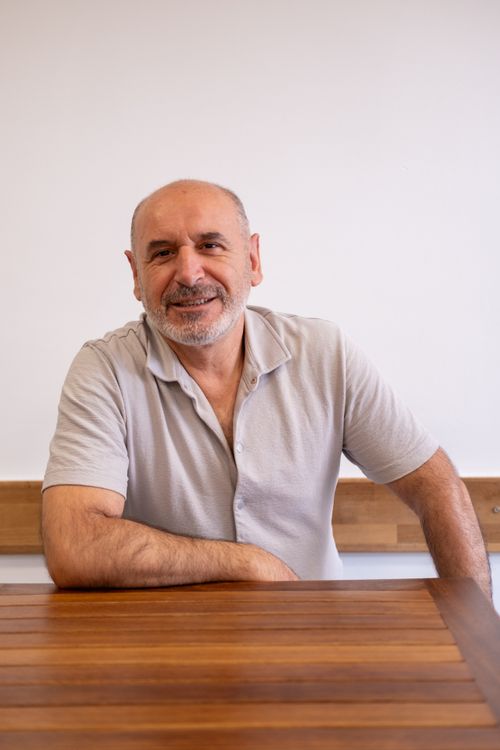 Free A cheerful mature man with a beard sits at a wooden table, exuding warmth and friendliness. Stock Photo