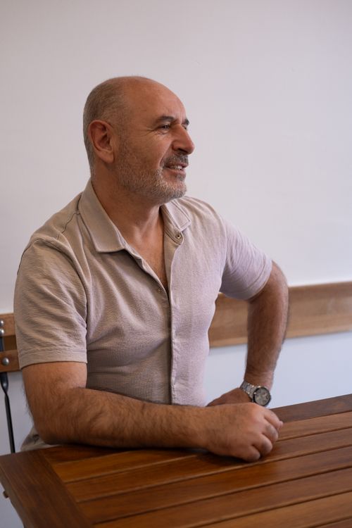Free A relaxed Caucasian man smiling while sitting at a wooden table indoors, captured in natural light. Stock Photo