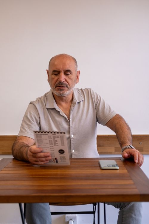 Free Senior man reading a menu in a cozy Izmir café, contemplating his order. Warm ambiance. Stock Photo