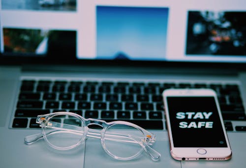 High angle of modern cellphone with Stay safe on screensaver and netbook with glasses placed above