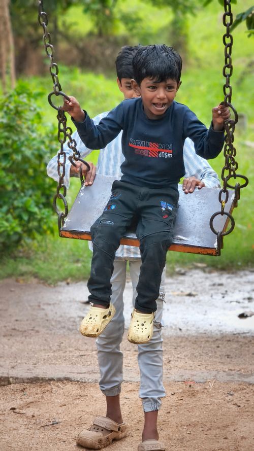 Free Two young boys enjoying a swing ride outdoors in Bhavanisagar, India. Joyful childhood moment. Stock Photo