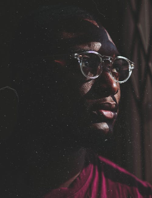 Serious portrait of a man with eyeglasses in low light, exuding a thoughtful mood.