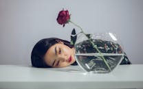 一幅优雅的肖像画中，女子将头靠在插有红玫瑰的花瓶旁，宁静与美丽之感油然而生