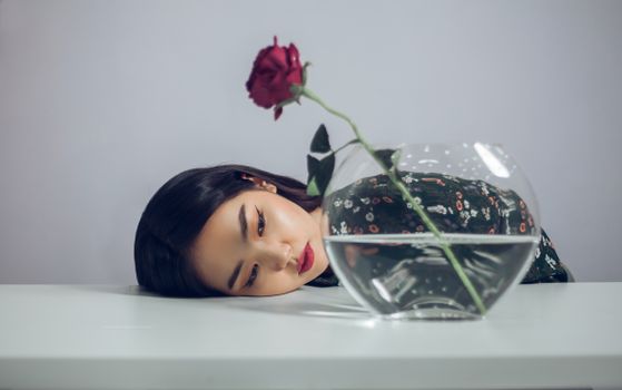 一幅优雅的肖像画中，女子将头靠在插有红玫瑰的花瓶旁，宁静与美丽之感油然而生
