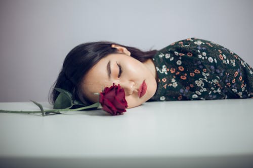 Melancholy ethnic woman with red rose on table