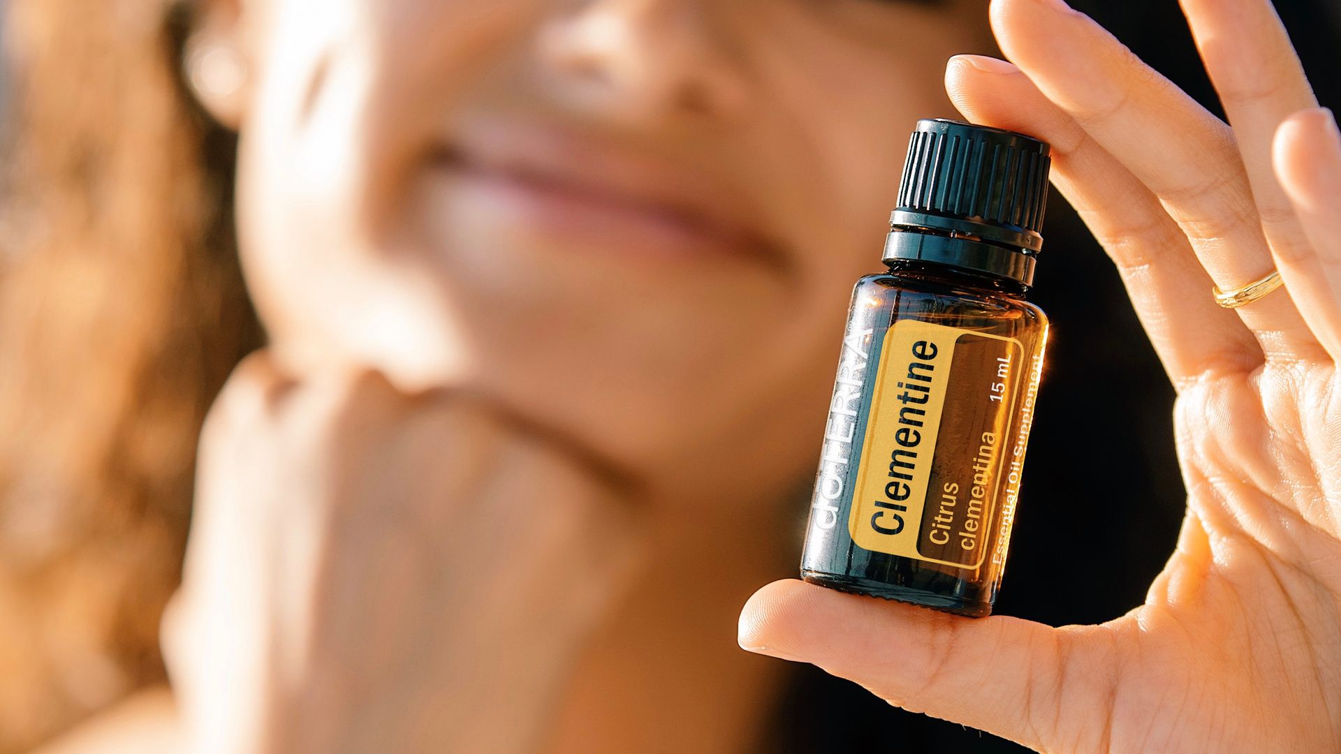 A close-up image of a woman holding a Clementine essential oil bottle, highlighting natural skincare.