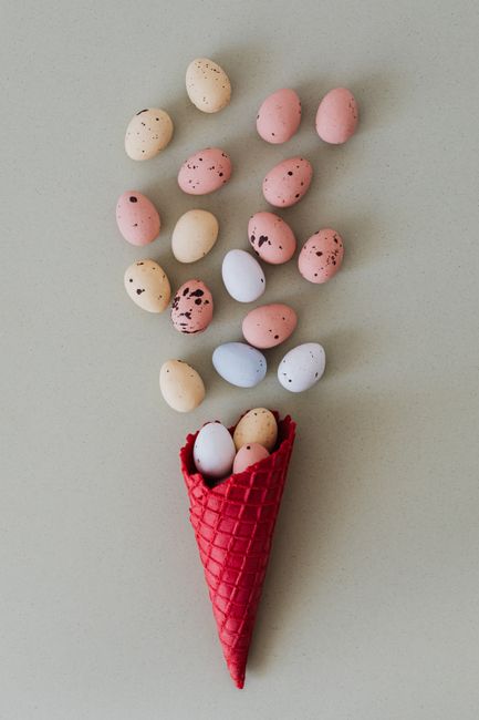 Artistic arrangement of colorful Easter eggs and red cone on a soft pastel background.
