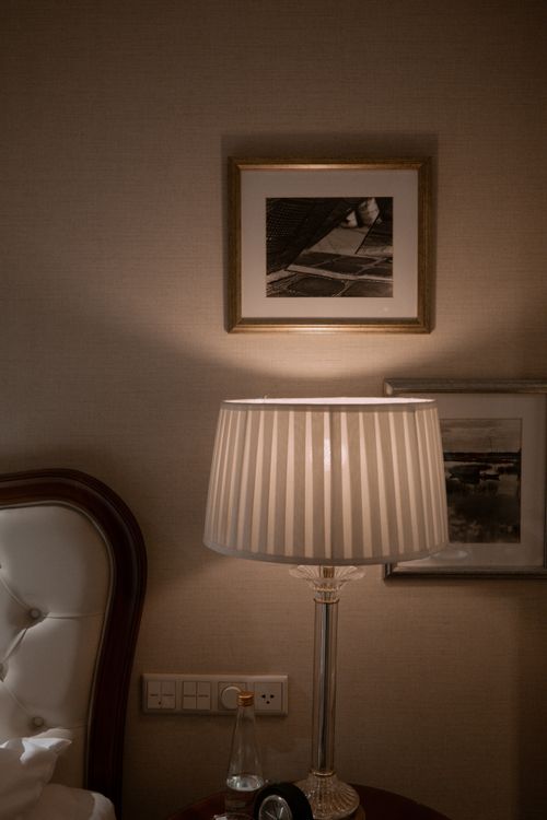 Free Warmly lit bedroom scene with elegant lamp and framed wall art, creating a cozy ambiance. Stock Photo