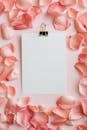 Top view of clipboard in pink petals of roses frame arranged on pink table