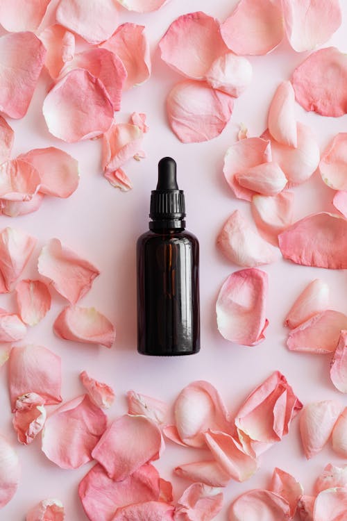 Top view of glass brown jar with pipette placed on pink table with petals of roses