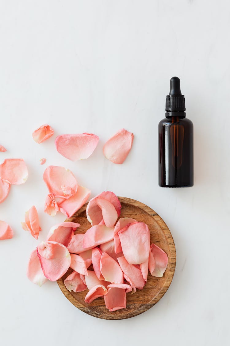 Essence Bottle With Pile Of Rose Petals On Wooden Plate