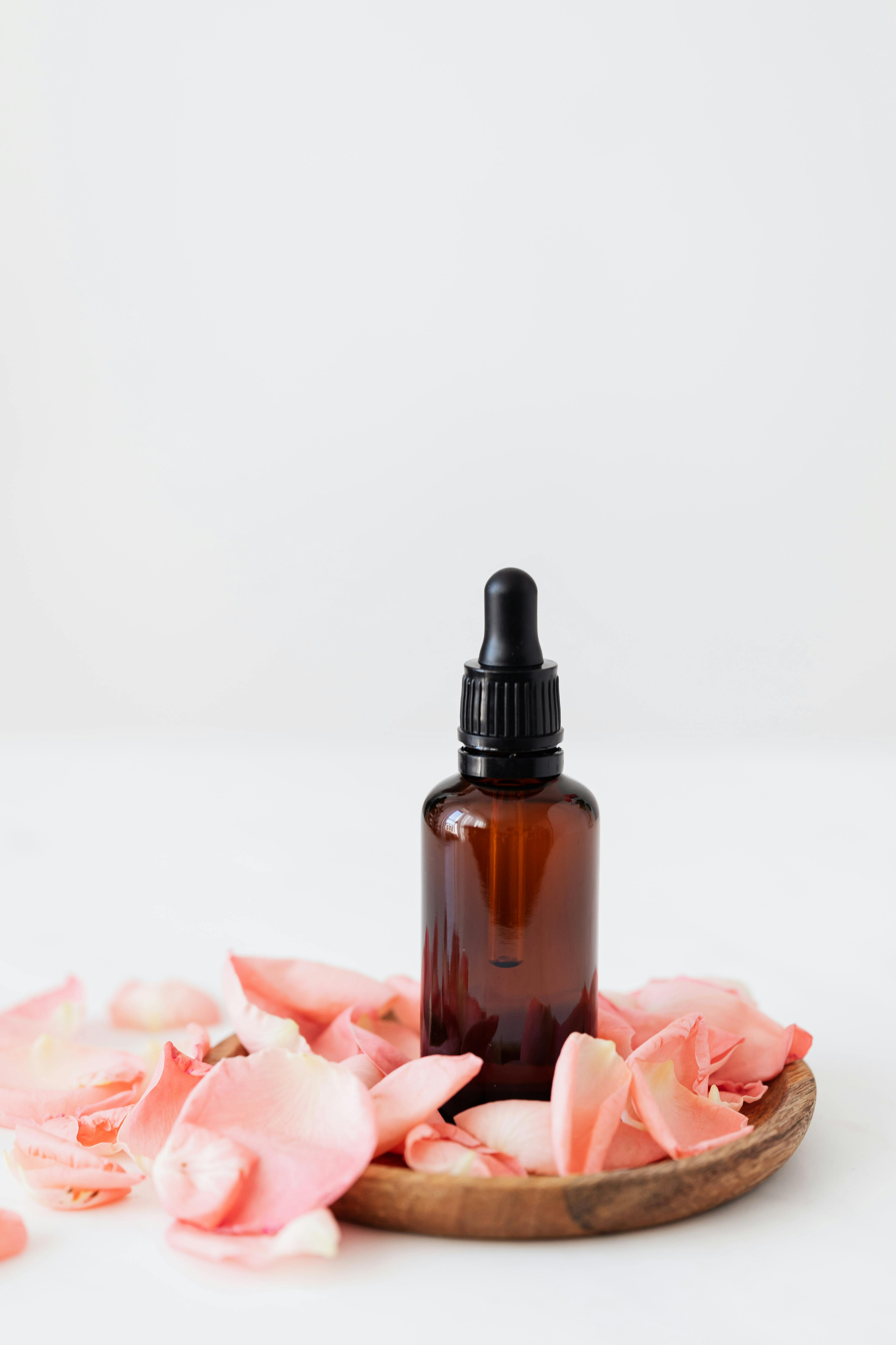 small essence bottle with rose petals on wooden plate