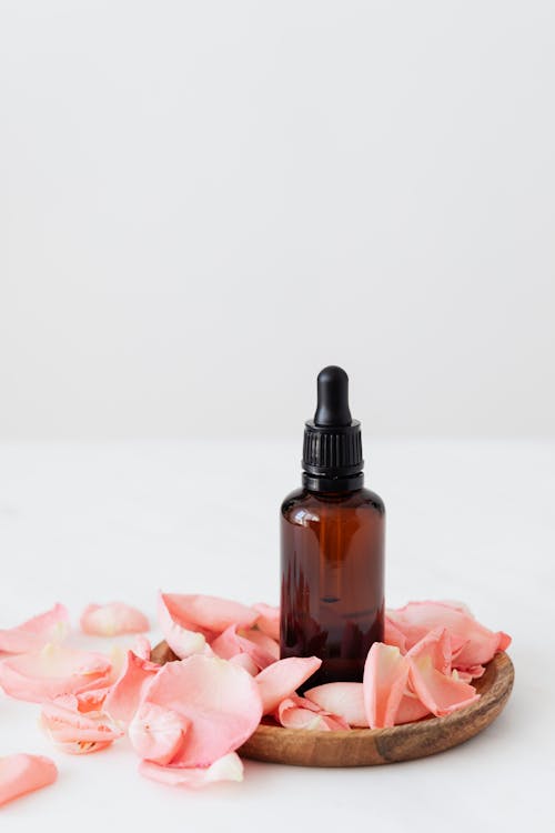 Transparent essence bottle on wooden plate with rose petals