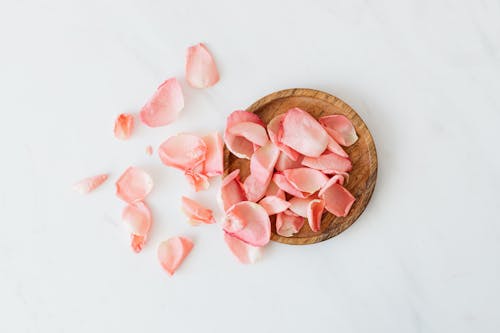 Free Top view of delicate pink rose petals placed in wooden bowl and near it on white surface as romantic date and celebration concept Stock Photo