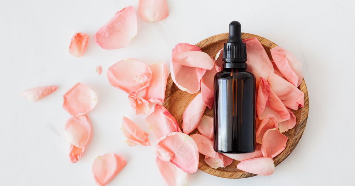 Dark amber serum bottle with dropper on a wooden dish surrounded by pink rose petals