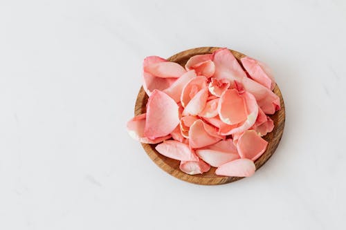 Delicate rose petals and wooden plate on white background