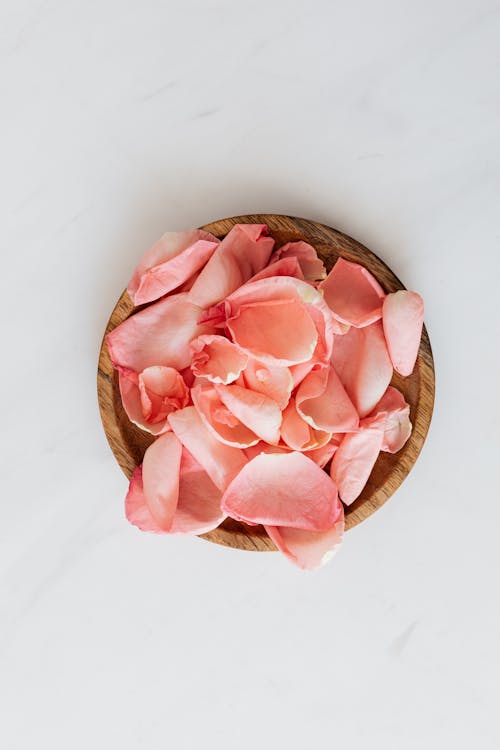 Delicate rose petals and wooden plate on white surface