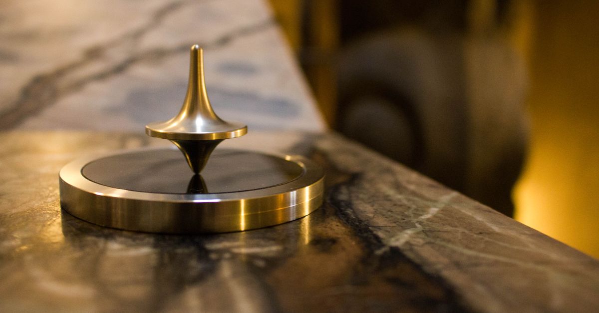 A close-up of a spinning top on a table, with a blurred background suggesting uncertainty