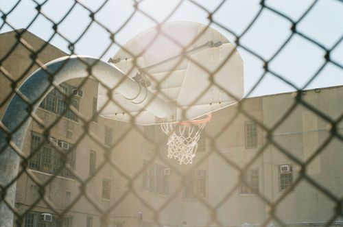 Free Vintage basketball hoop in urban playground, seen through a chain-link fence on a sunny day. Stock Photo
