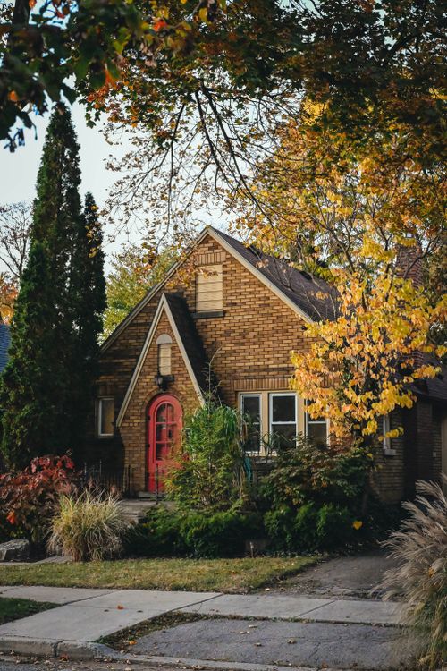 Free Serene image of a brick house surrounded by vibrant autumn foliage, offering a cozy suburban feel. Stock Photo