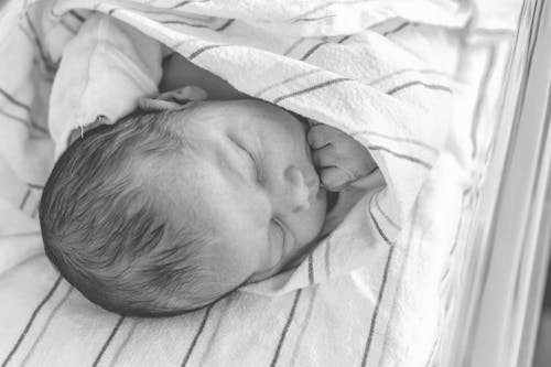Black and White Photograph of a Newborn Baby Lying on a Striped Textile