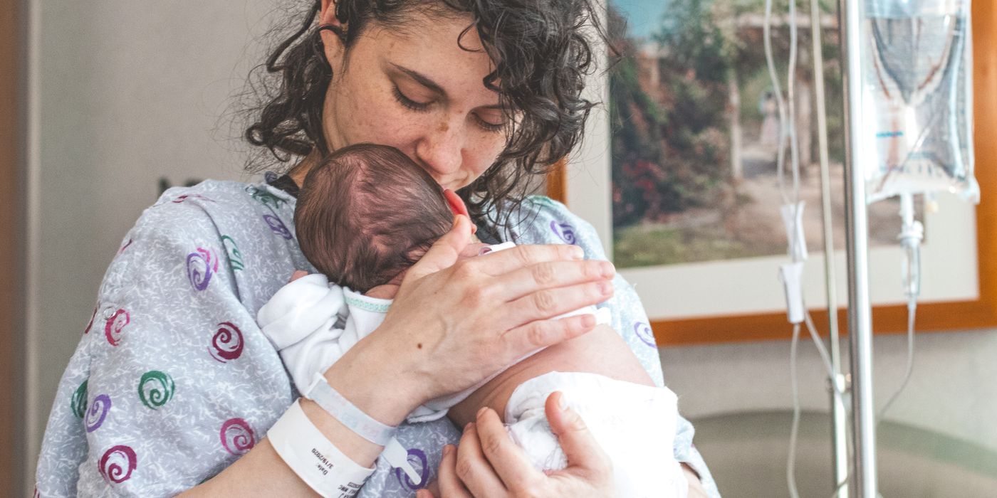 Mother gently holding newborn baby in hospital setting, showcasing warmth and love.