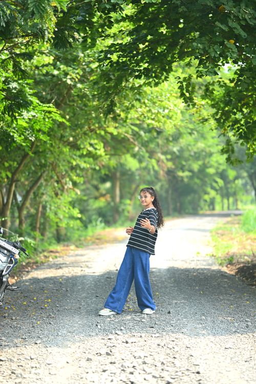 Free A young girl enjoying a playful walk along a sunlit, forested pathway. Stock Photo