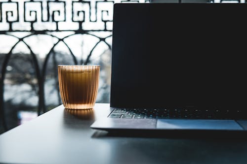 Free Netbook on black table with glass of drink against balcony fence in sunlight Stock Photo