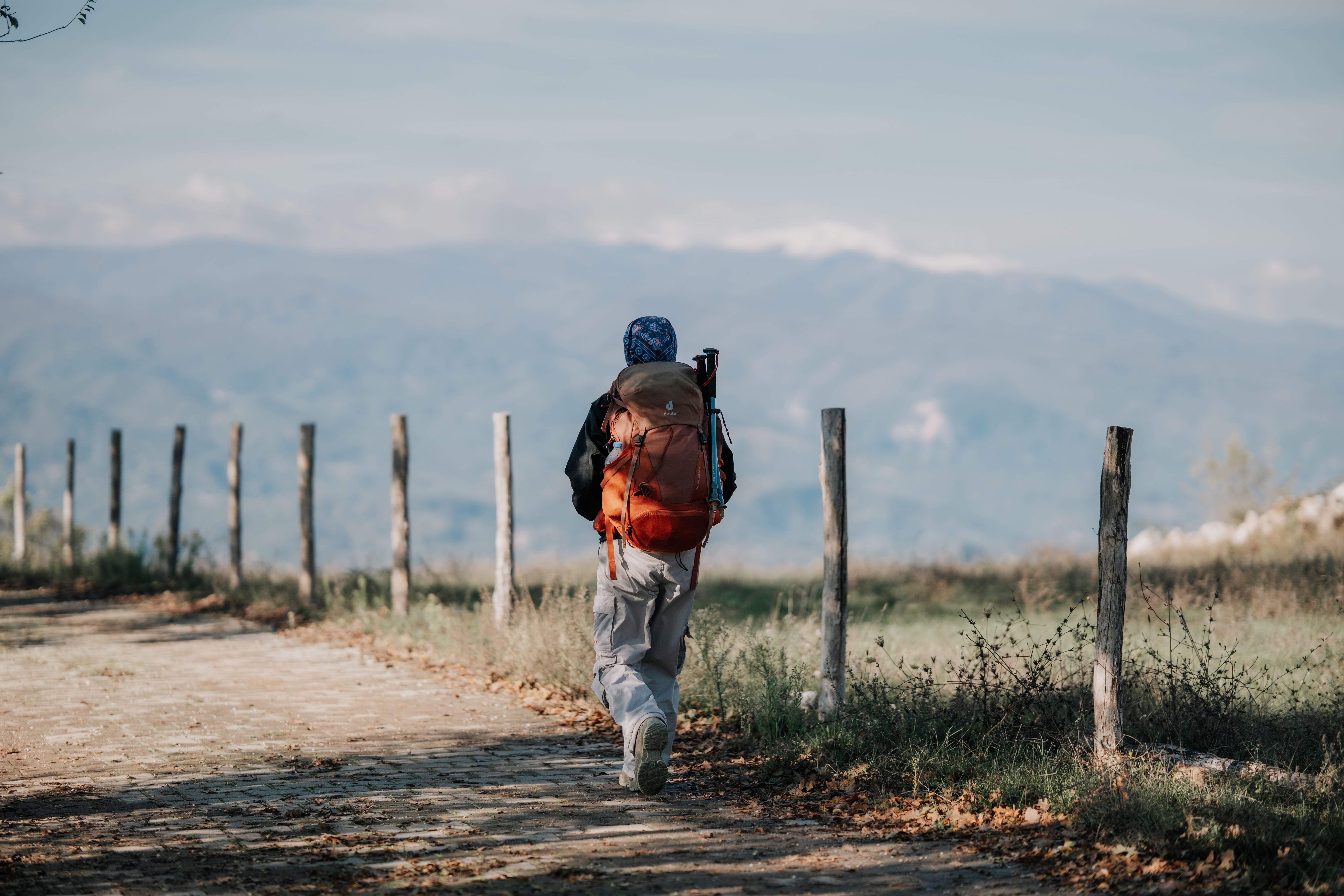 A lone backpacker walks along a rustic path with scenic mountain views, perfect for adventure travel themes.