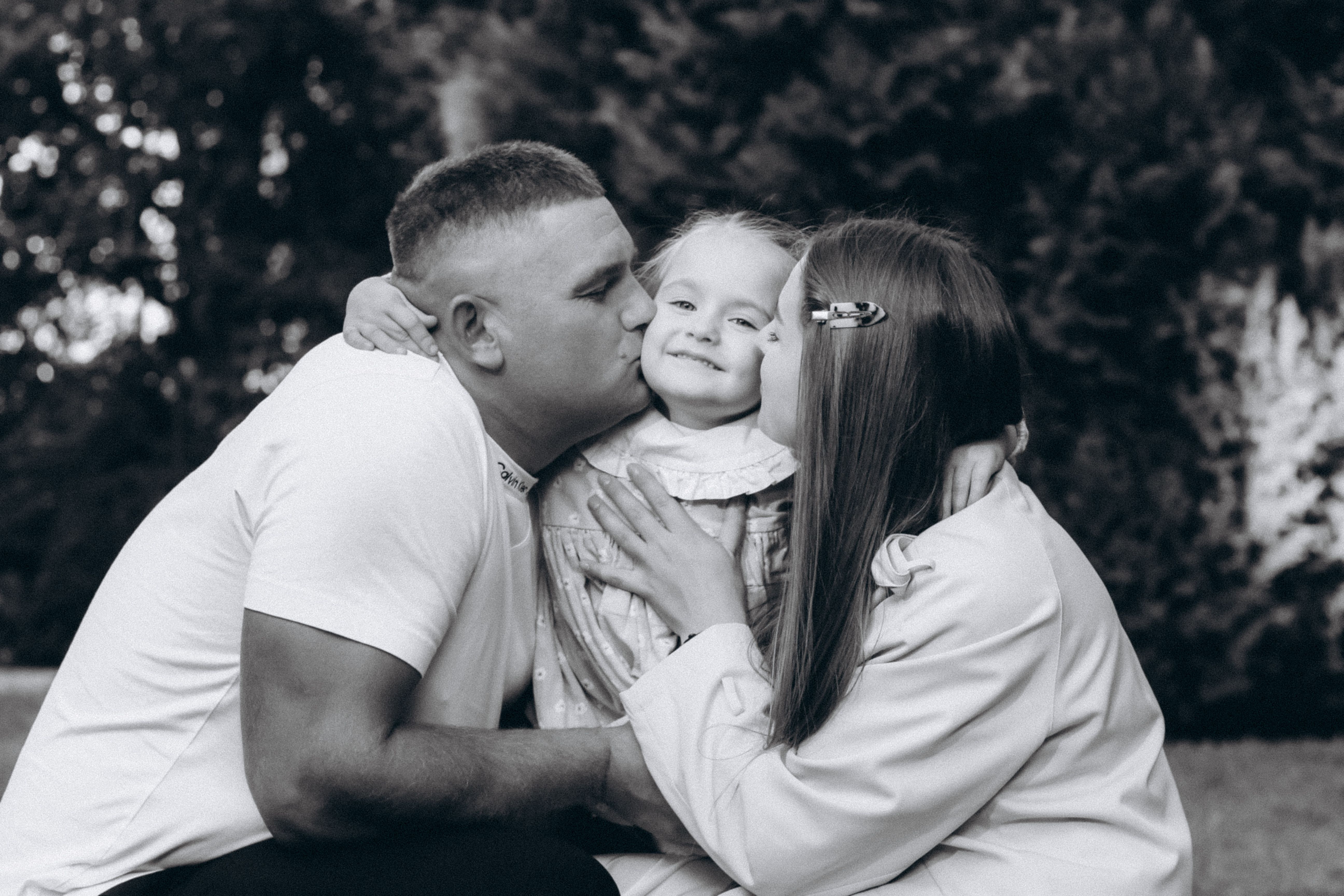 A family shares a tender moment in a garden in Wrocław, Poland, showcasing love and togetherness.